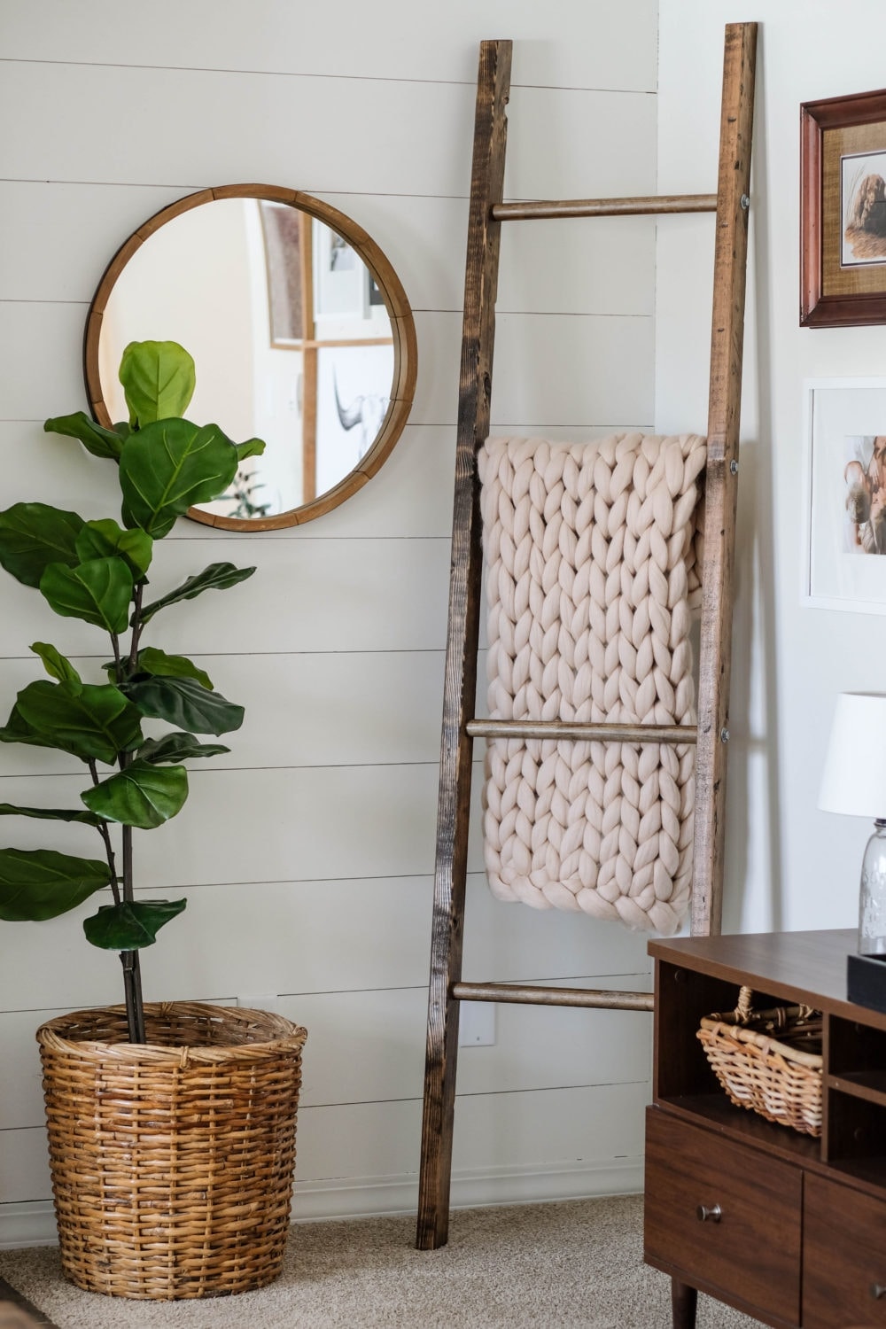 Blanket ladder with chunky knit blanket on one rung next to a round mirror and fiddle leaf fig tree