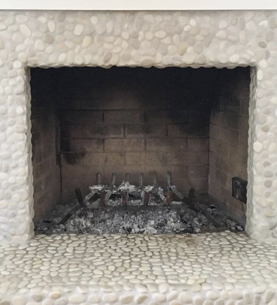 Empty fireplace opening with ashes inside and small pebble rocks surrounding it