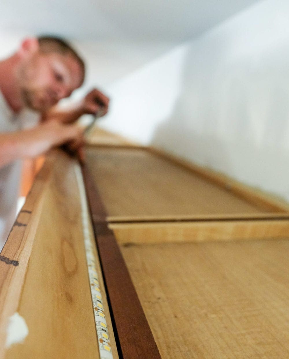 an LED light strip being applied to the top of a cabinet in a kitchen