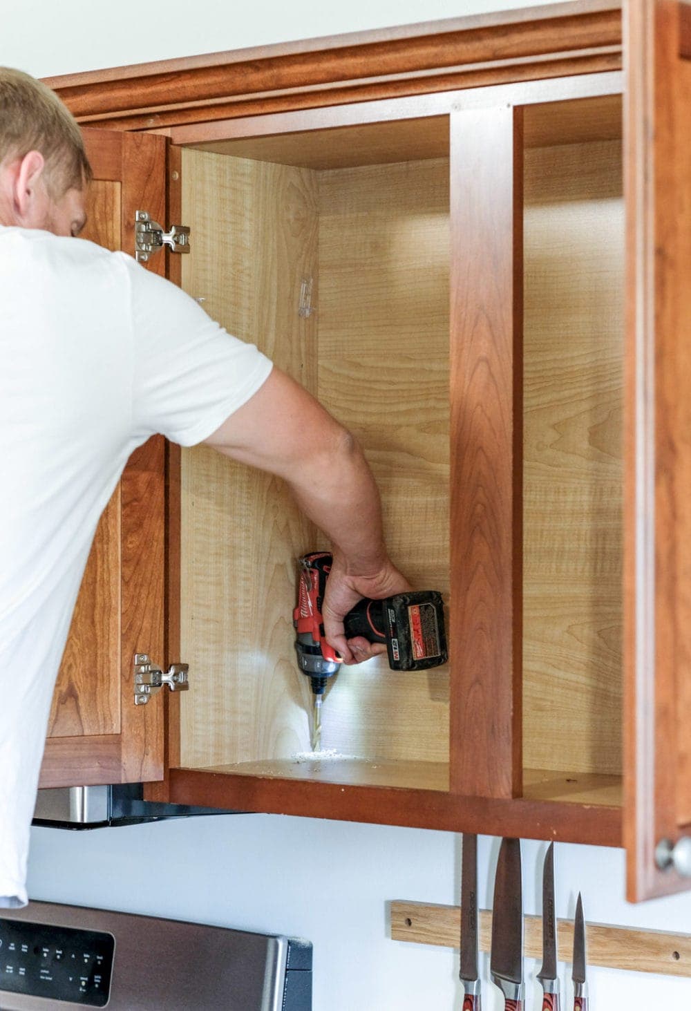 drilling a hole through the bottom of a kitchen cabinet to install wires for lighting