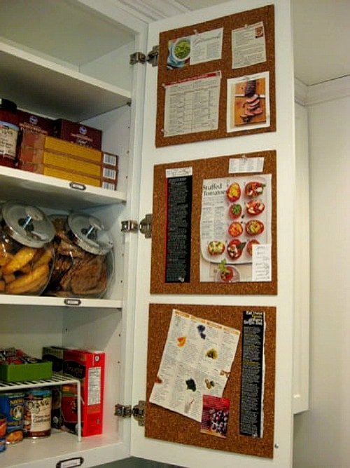 Open kitchen cabinet with cork boards glued to the inside of the door with recipes and sticky notes pinned to the board