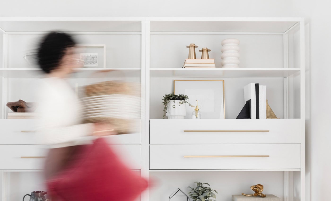 woman puts items on shelf in living room - shelf styling tips how interior designer curate shelves