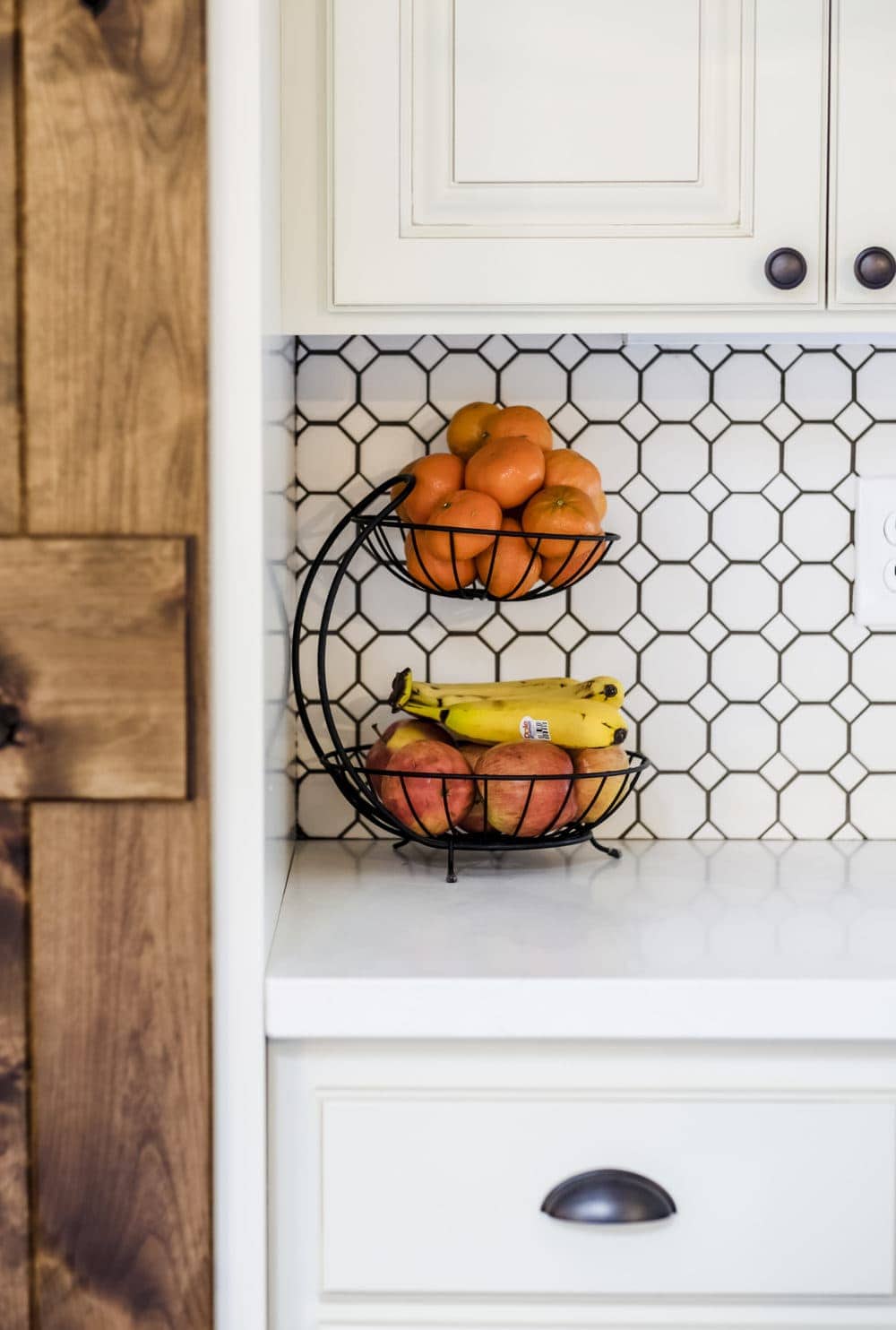 Black stacked fruit basket with oranges and bananas against white penny tile backsplash