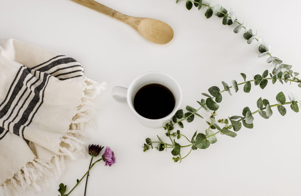 white solid surface countertops with a cup of coffee, a dishtowel and eucalyptus leaves