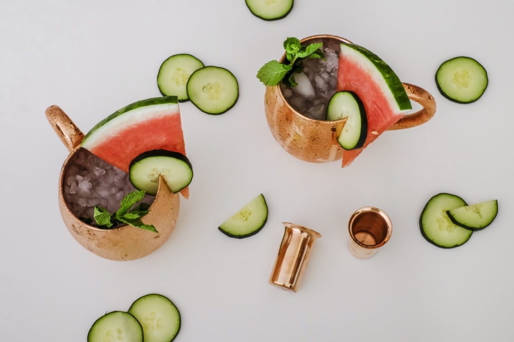 View looking down on two copper mugs filled with cucumber watermelon moscow mule ingredients 