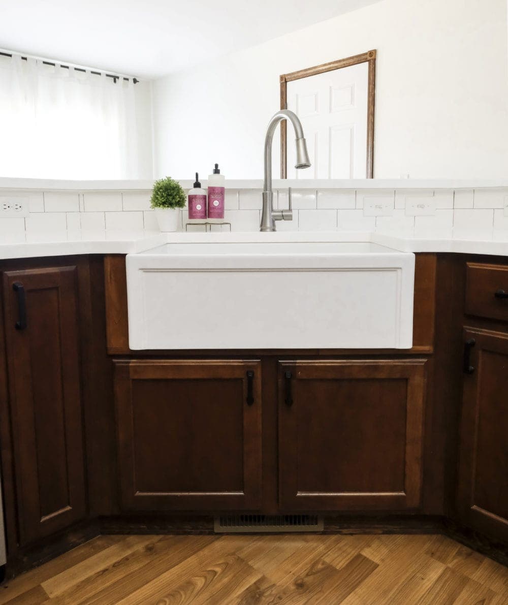 A white fireclay farmhouse sink with white counters and wood cabinets