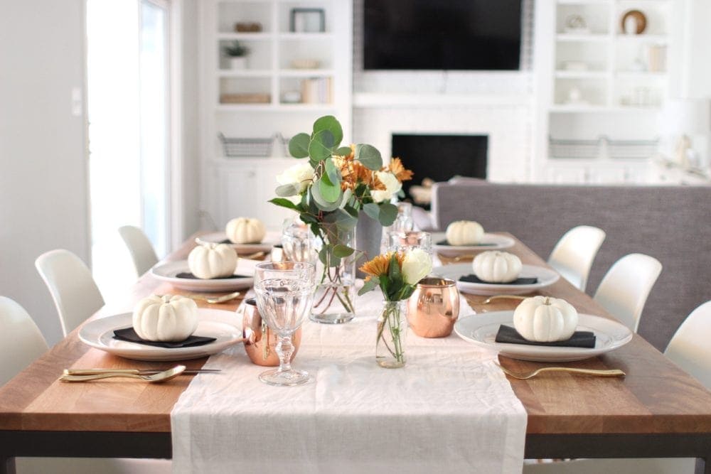 Thanksgiving table centerpieces with white mini pumpkins, a natural table runner and copper mugs