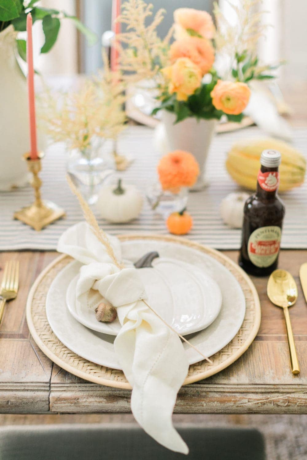 Thanksgiving table centerpieces with mini pumpkins, gold candleholders and white napkins tied with a wheatstock