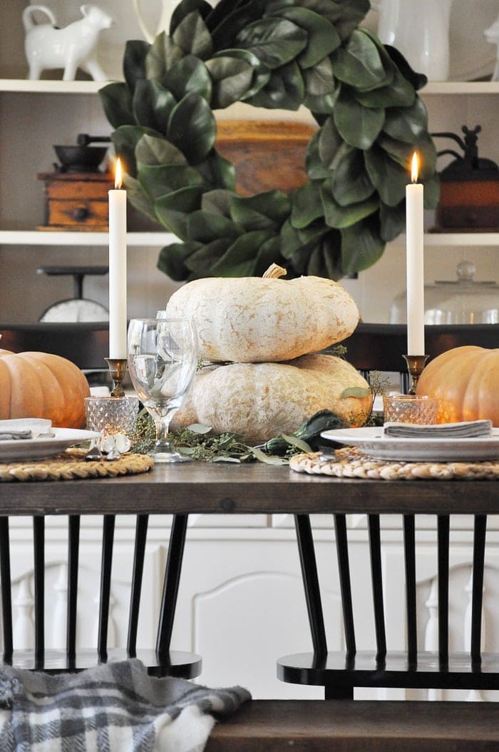 Thanksgiving table centerpieces with stacked white pumpkins in between two tall candlesticks