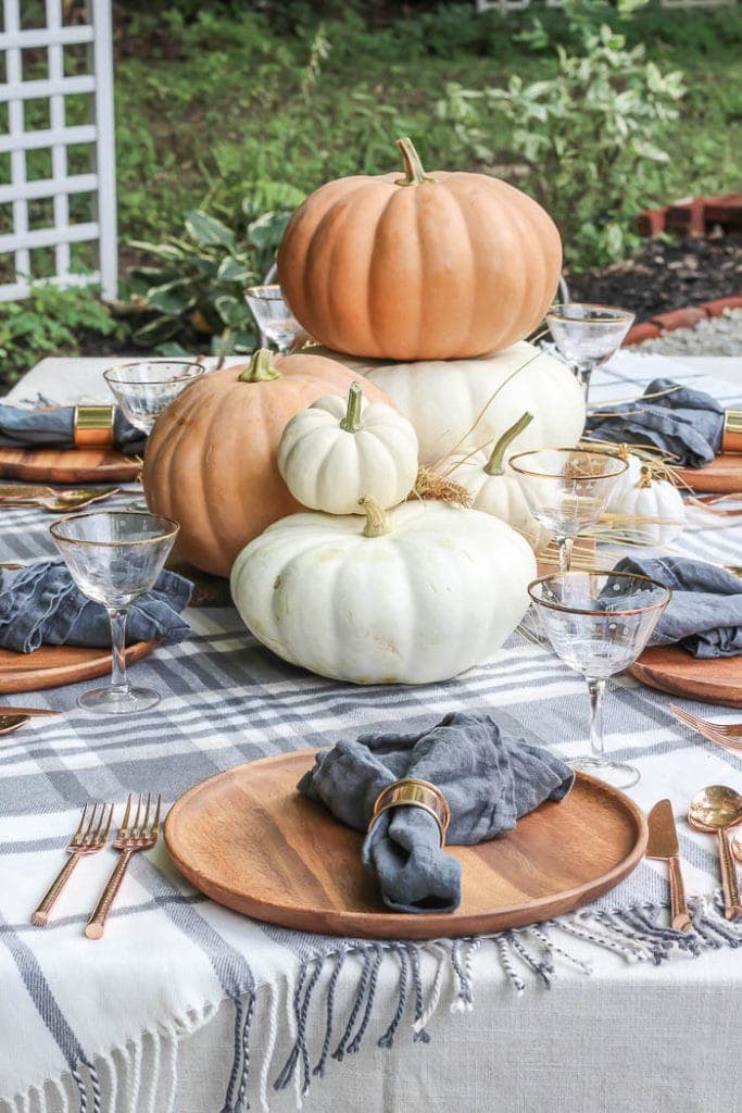 Thanksgiving table centerpieces with plaid tablecloth and large pumpkins next to wood chargers