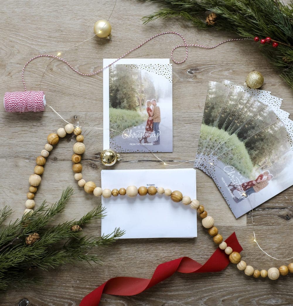 Overhead view of a personalized Christmas card layed out with ribbon, garland, and greenery