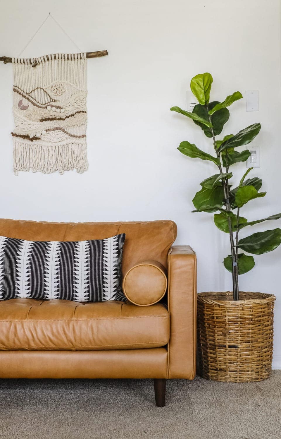 Leather sofa with black throw pillow next to an artificial fiddle leaf fig tree