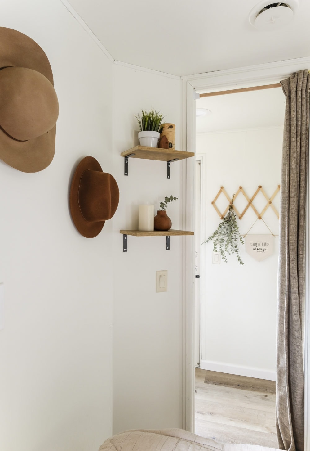 RV bedroom with 2 small shelves and hats hanging on the wall