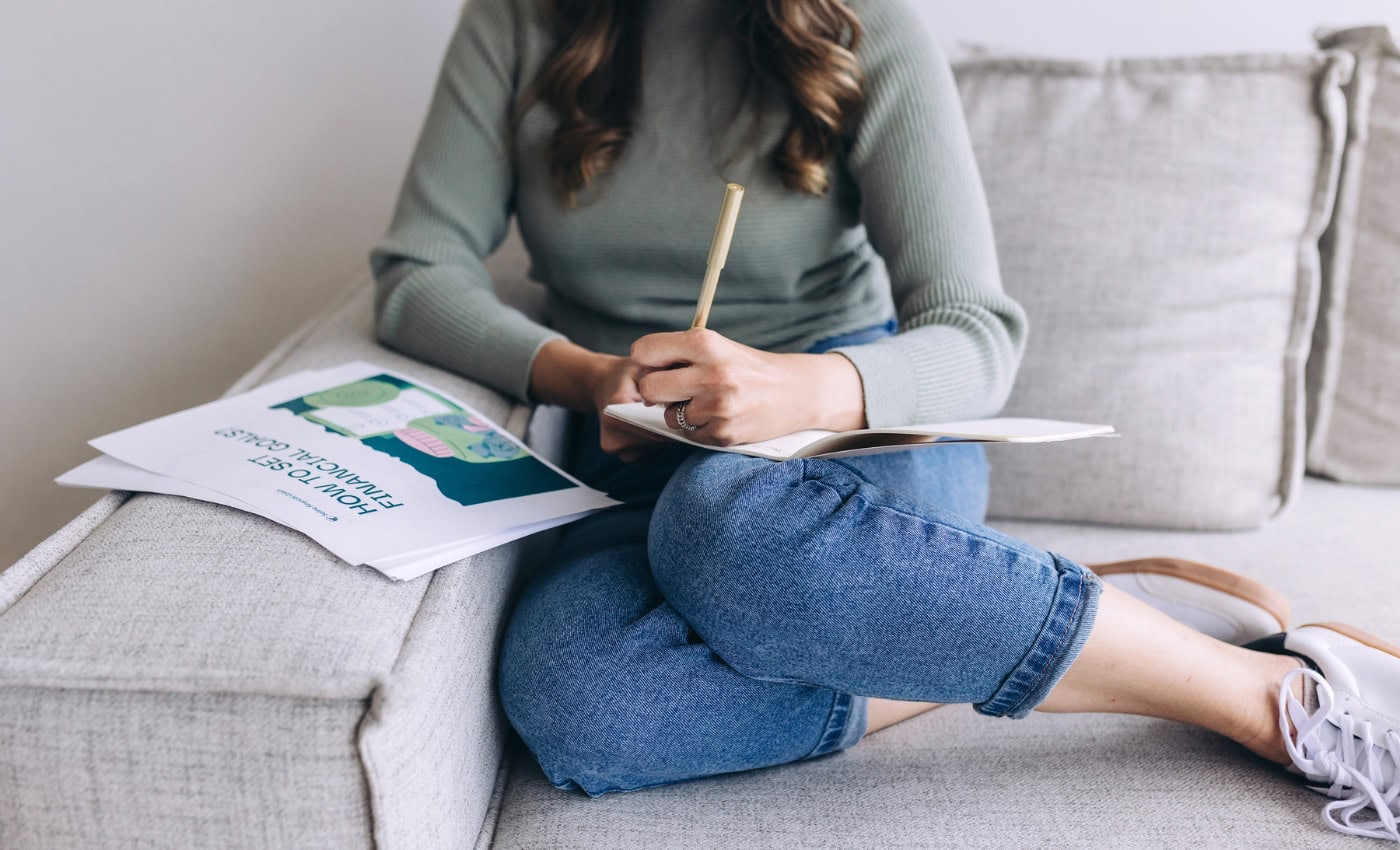 woman puts notes in her financial goals planner as she learns 17 Ways To Drastically Cut Household Expenses