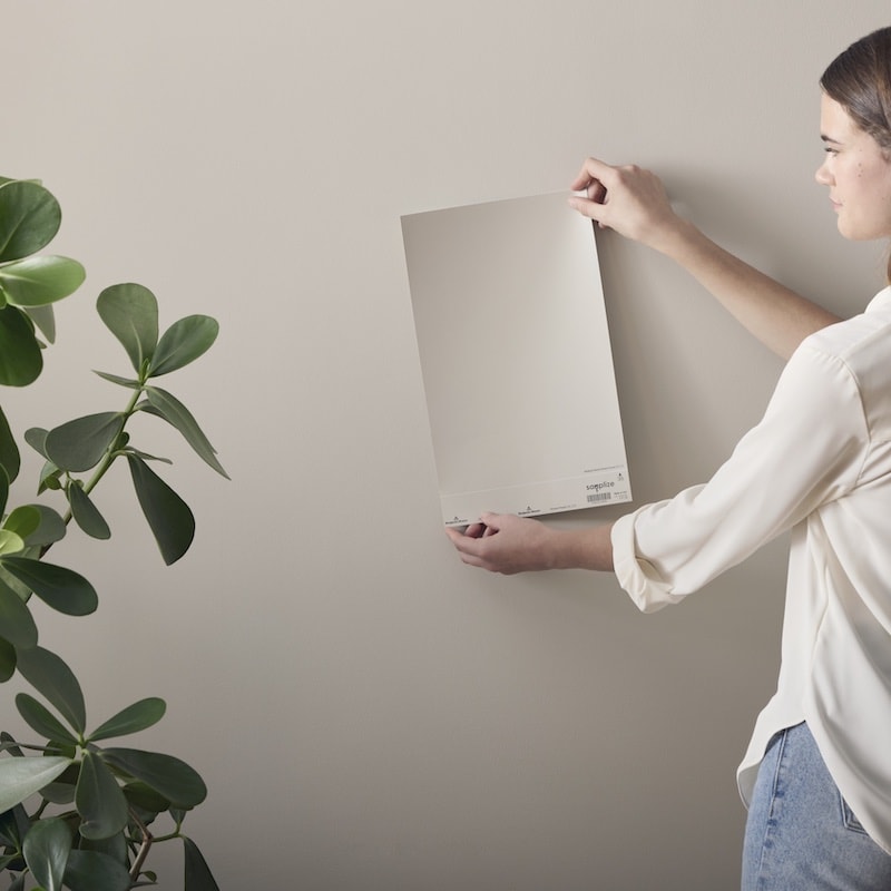 woman holding up a Samplize paint color sample against a wall 