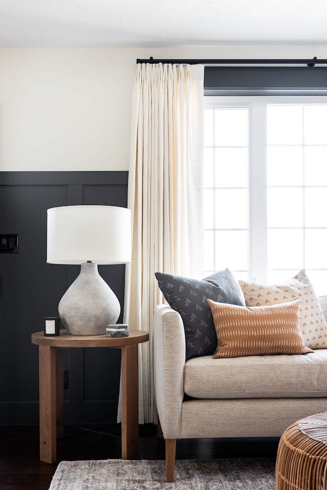 Living room with black wall paneling, White Dove on walls above with gray sofa and side table with lamp